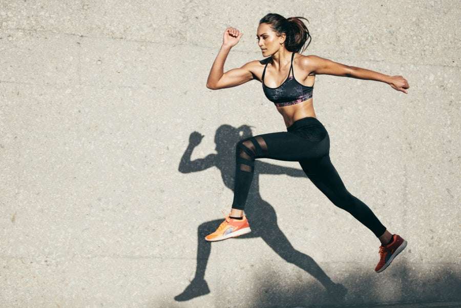 Shilajit Vital Gummies con una atleta en ropa deportiva negra y zapatillas naranjas, saltando enérgicamente